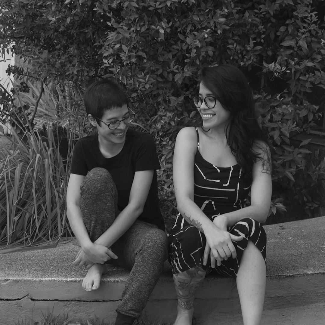 fotografia preto e branco das integrantes da oficina cigarra, sentadas em rampa de concreto com vegetação ao fundo.